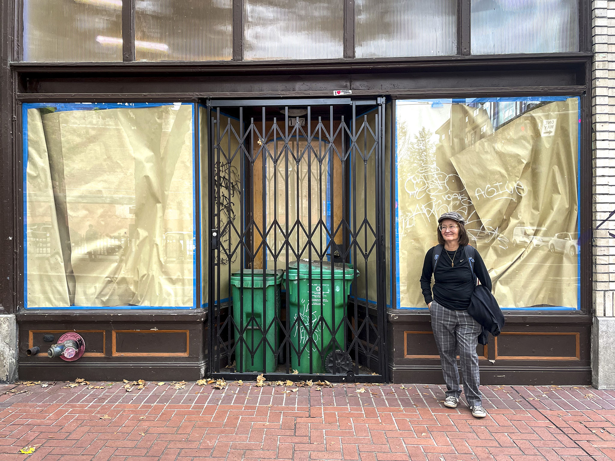 Barbra Weber stands in front of the former building for the Sisters of the Road cafe, which is locked up with a metal gate and has brown paper and painters tape lining the windows. 