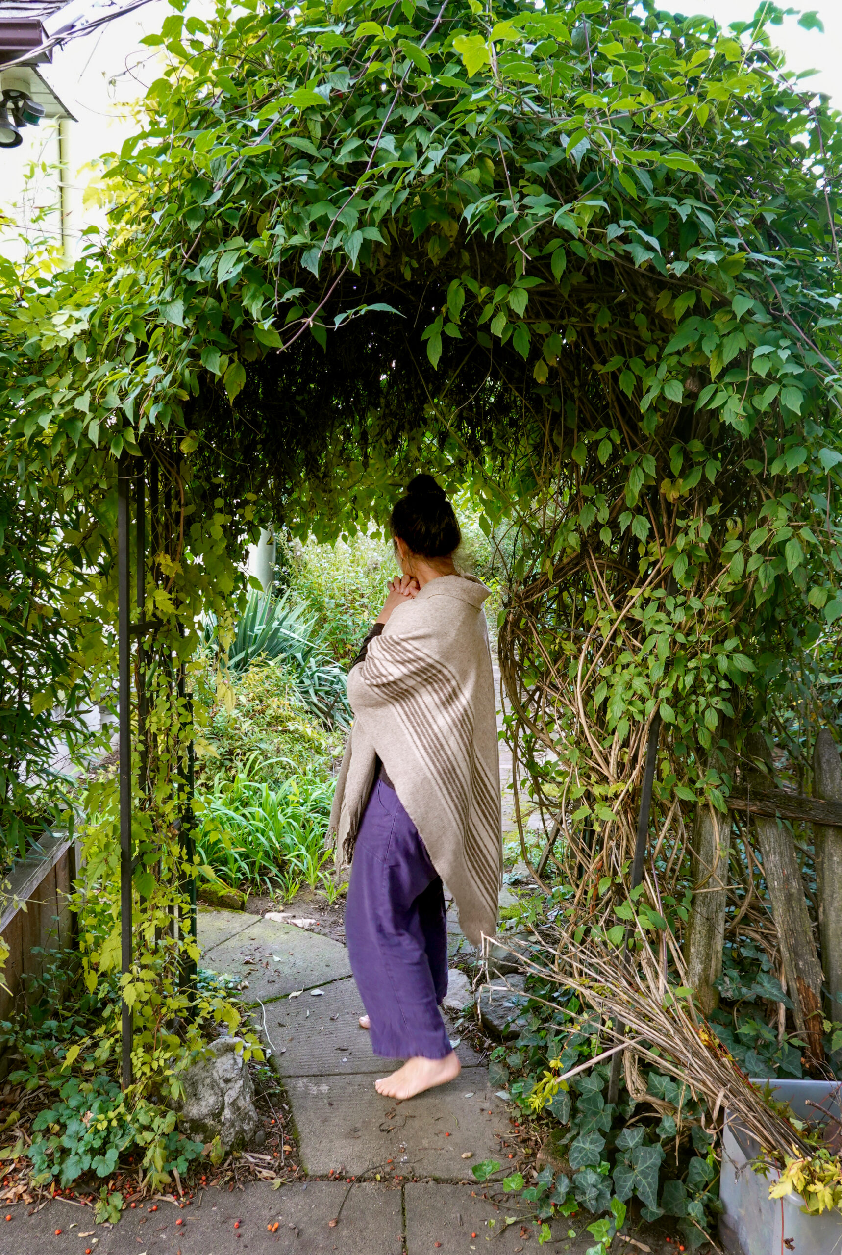 Green is seen from the back as she stands under a leaf-covered arch. 