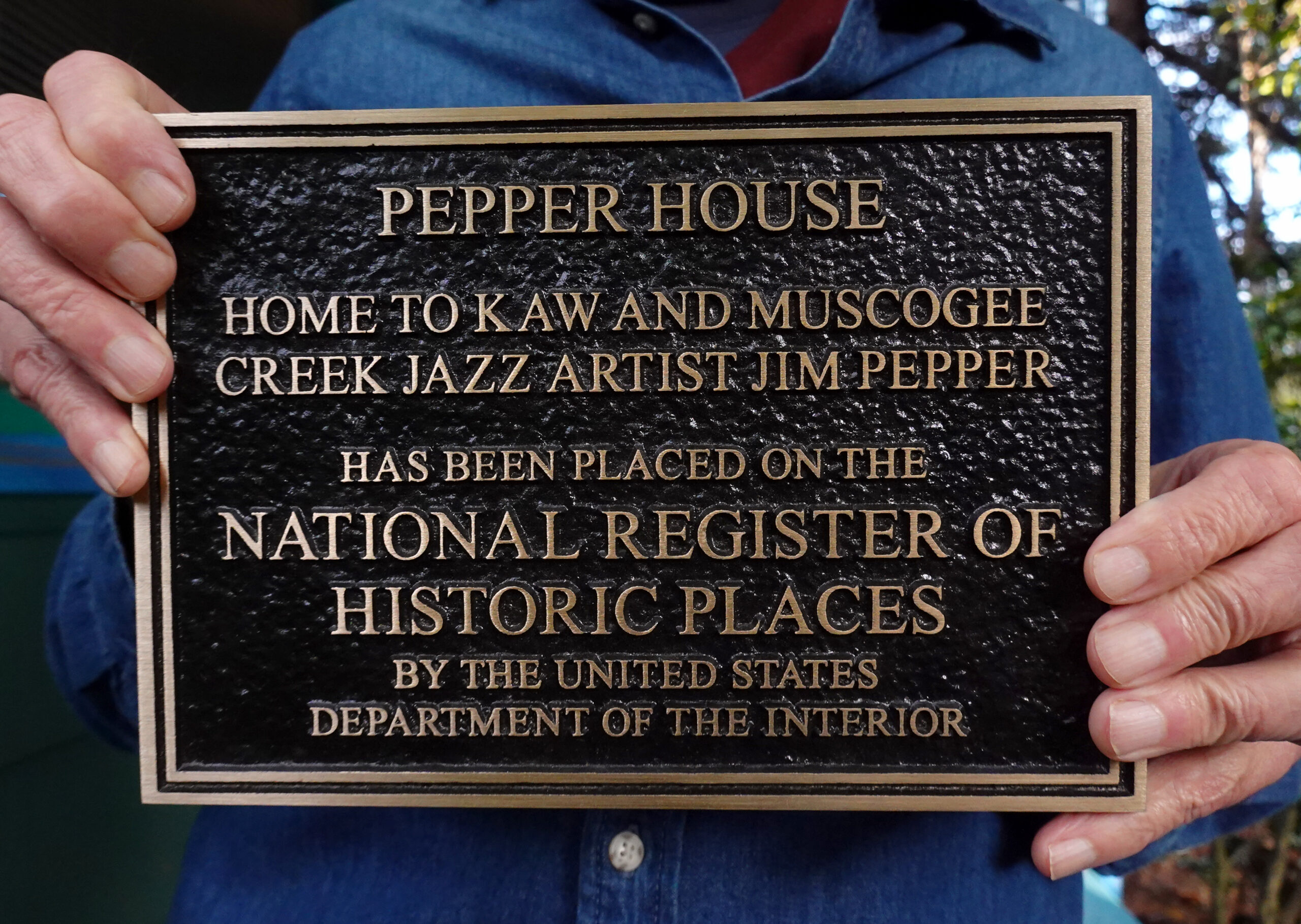 Sean Cruz holds a plaque from the Department of Interior listing the former home of Jim Pepper on the National Register of Historic Places. The plaque reads, “Pepper House. Home to Kaw and Muscogee Creek Jazz Artist Jim Pepper.”